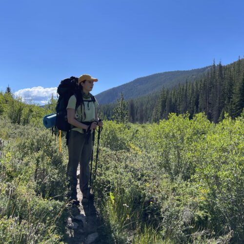 A girl wearing a backpack looks out at the Rocky mountains